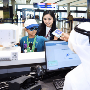 A young boy with his guardian standing in front of a screen showing Hidden Disabilities Sunflower logo at Dubai International Airport (DXB).